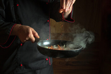 Professional chef adds dry fragrant spices to a hot pan. Roasting onions with carrots before...