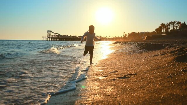 Child boy silhouette running on beach at sunset. Kid running on water at ocean beach at sunset. Boy having fun in holiday vacation with sun light. Youth, lifestyle and happiness concept.
