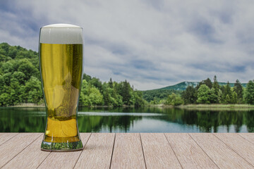 Glass of light beer on table with view of forest with lake