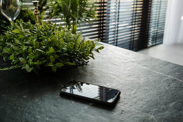 Mobile phone on a table. Black cellphone on the table. A single mobile phone on wooden table in the office. Electronic devices. Smart phone on table with bright morning window light streaming through.