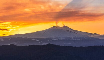 mysterious landscape of great erupting volcano with smoke from craters and snow on slopes in orange...