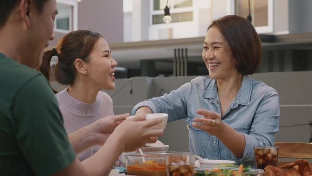 Mom enjoy thai meal cooking for family day home dining at dine table cozy patio. Mum passing serving food to group four asia people young adult man woman friend fun joy relax warm night picnic eating.