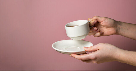 Female hands holding a cup of tea and a saucer on a pink background