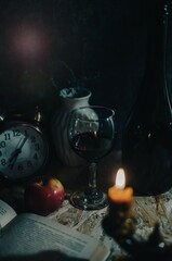 An open book, a glass of wine, a clock at dusk by candlelight