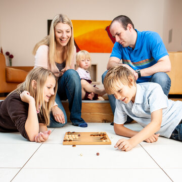 Family Life, Friendly Fun. A young family enjoying time together at home with a simple board game. From a series of related images.