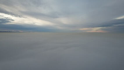 Fototapeta na wymiar A heavenly ocean of clouds. Flying on a drone. The light yellow rays of the sun at sunset are reflected on the surface of the clouds. Double layer of clouds and heavy fog. Evening. Kazakhstan