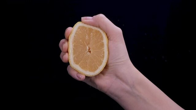 Woman squeezing a lemon half on black background. Citrus fruit source of vitamins and health concept. Slow motion