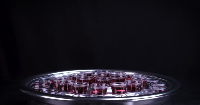 Communion glass cups on tray filled with wine the symbol of Jesus Christ blood on black background. Easter Passover and Lord Supper concept. Dolly shot 4k