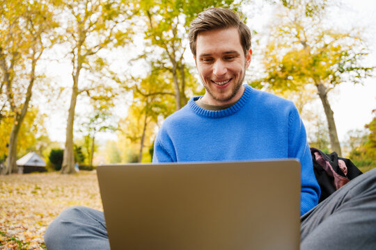 Cheerful man working on laptop while sitting in park