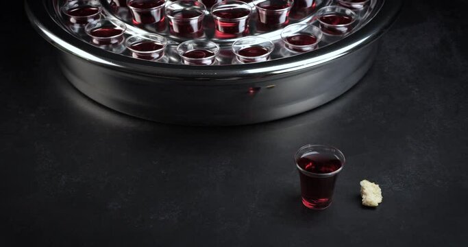 Communion glass cups on tray filled with wine the symbol of Jesus Christ blood on black background. Easter Passover and Lord Supper concept. Dolly shot 4k