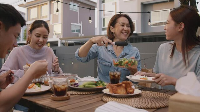Mom enjoy thai meal cooking for family day home dining at dine table cozy patio. Mum passing serving food to group four asia people young adult man woman friend fun joy relax warm night picnic eating.
