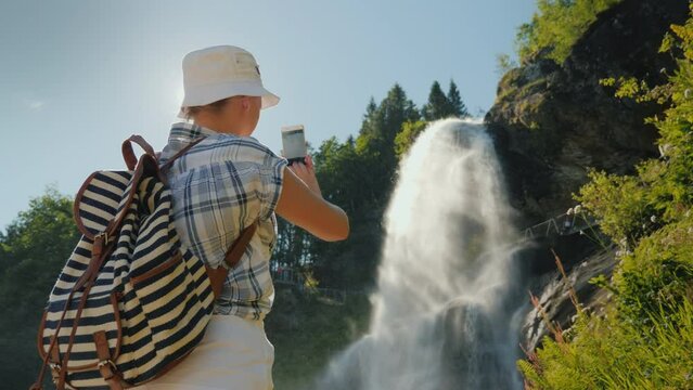 Woman using smartphone takes pictures of majestic Steinsdalsfossen is a waterfall in the west of Norway