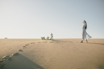 Woman with long hair in a stylish dress poses in the desert sands.