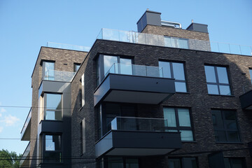 Fototapeta premium Modern residential building with balconies and dark brick facade. Real estate and housing issues concept.