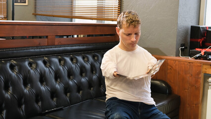 a young man with disabilities is looking at a catalog when choosing a hairstyle in a barber shop