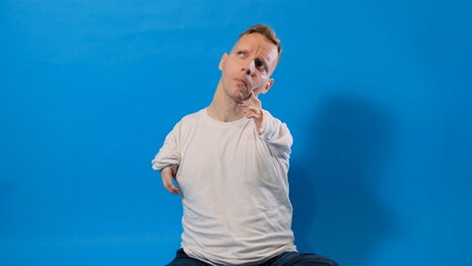 a man with disabilities of congenital pathology of the hands looks up thoughtfully sitting on an isolated blue background.