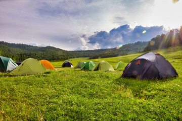 Tourist tent in the camp among the meadows in the mountains. Outdoor camping with beautiful sunshine in the morning - obrazy, fototapety, plakaty