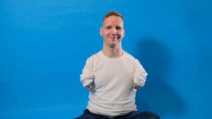 a smiling and cheerful man in a white T-shirt with disabilities sits on an isolated blue background.
