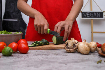 Cropped shot of hand cutting cucumber with various fresh vegetable at the kitchen. 