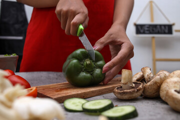 Cropped shot of hand cutting green paprika with various fresh vegetable at the kitchen. 