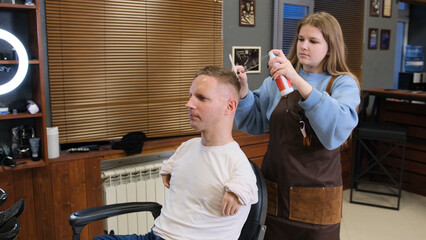 the girl master in the barber shop conducts hair styling for a man with disabilities sitting in a...