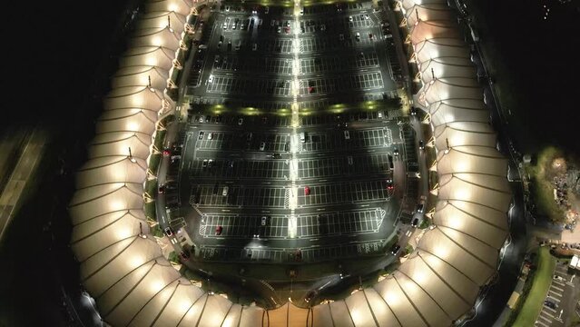 Aerial view tilt up over McArthur Glen illuminated nighttime luxury designer shopping outlet and car park, Ashford, Kent