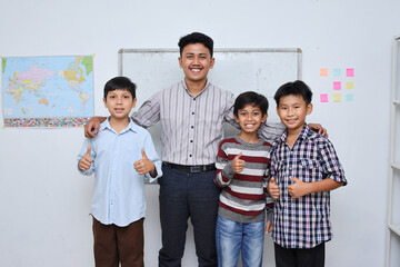 Smiling schoolboy and teacher standing together in front of the classroom, looking at camera and giving thumbs up . Banner for Teacher's Day.