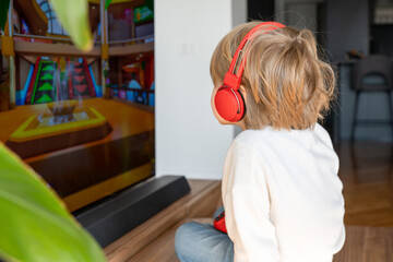Side view image of cute little blond hair boy sitting on a table and watching TV.