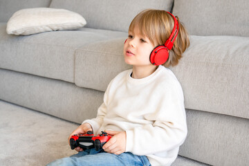 Little boy playing video game console using joystick or controller while sitting at home real...