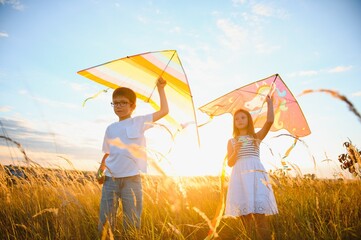 Happy boy and girl playing with kites in field at sunset. Happy childhood concept.