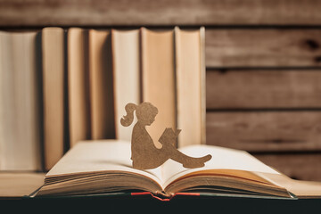 An introvert girl reads a book against a wooden background and stack of books