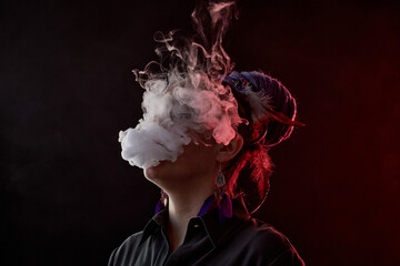 Thick cloud of white vapor hiding face of young smoking woman in casualwear standing in front of...