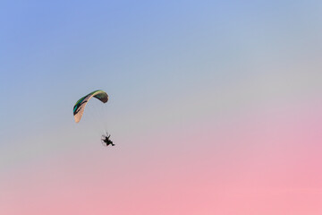 One paraglider flies in the sky at sunset.