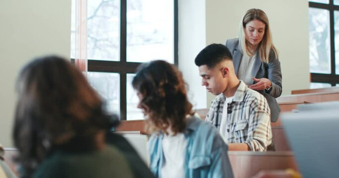Diverse students sitting at lesson and studying. Inside. Female Caucasian handing out materials for test on background. Woman teacher giving papers with exam. Examination concept.