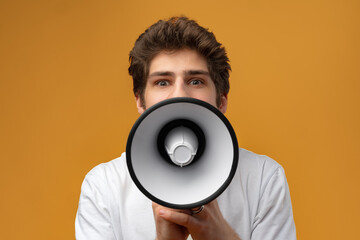 Young man shouting into megaphone making announcement against yellow background