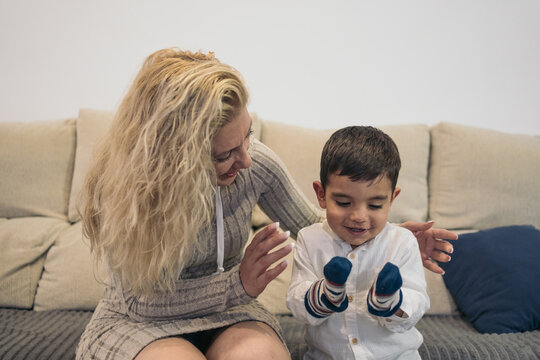 Middle-aged blonde woman teaching her young autistic son to play with socks in his hands as if they were puppets.