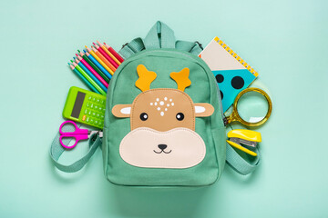 Back to school, education concept Deer backpack with school supplies - notebook, pens, eraser rainbow, numbers isolated on blue background Top view Copy space Flat lay composition