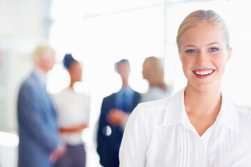 Smiling female professional with business team. Closeup of young female professional smiling with associates in background.