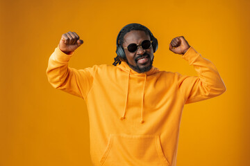 Young african man listening music with headphones isolated over yellow background.