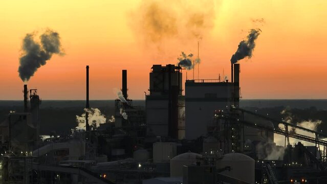 Aerial view of wood processing factory with smoke from production process polluting atmosphere at plant manufacturing yard. Industrial site at sunset