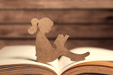 Paper silhouette of a little girl reading a book on a wooden background