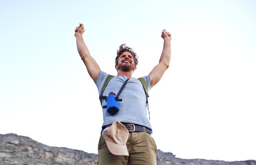 I made it. a handsome young man standing with his arms raised while hiking.