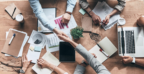 Top view of people working together and shaking hands while sitting at the desk in office