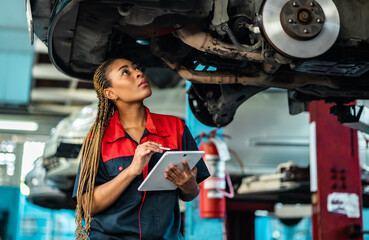 Engineer team checking under car condition on lifter in garage.Young auto mechanic in uniform is...