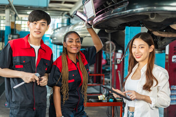 Asian and African  automotive engineer people wear helmet work in mechanics garage.young auto mechanic in uniform is looking at camera and smiling examining car...