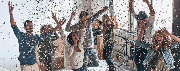 Cheerful young people dancing together and throwing confetti while having party at home