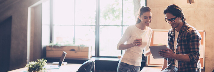 Two happy young people discussing business while standing in creative office together
