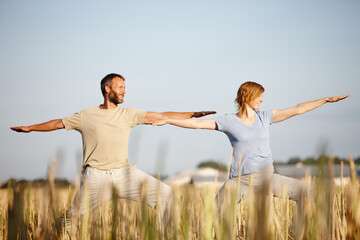 Boosting their well-being. a mature couple in the warrior position during a yoga workout in a field.