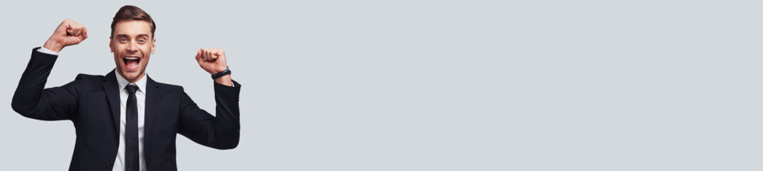 Excited young man in formal wear gesturing and smiling while standing against grey background