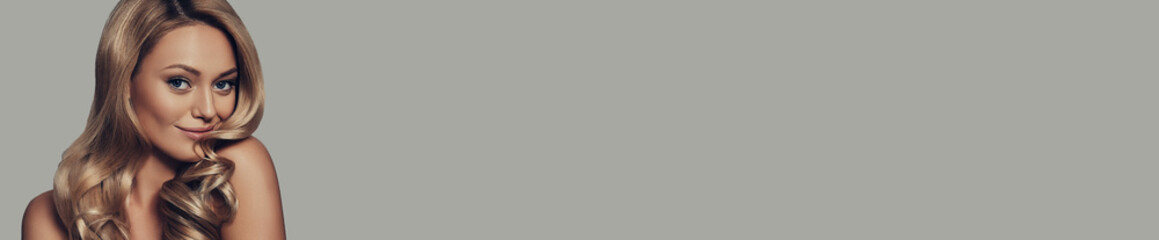 Naklejka premium Attractive young woman with long and waving blonde hair looking at camera against grey background